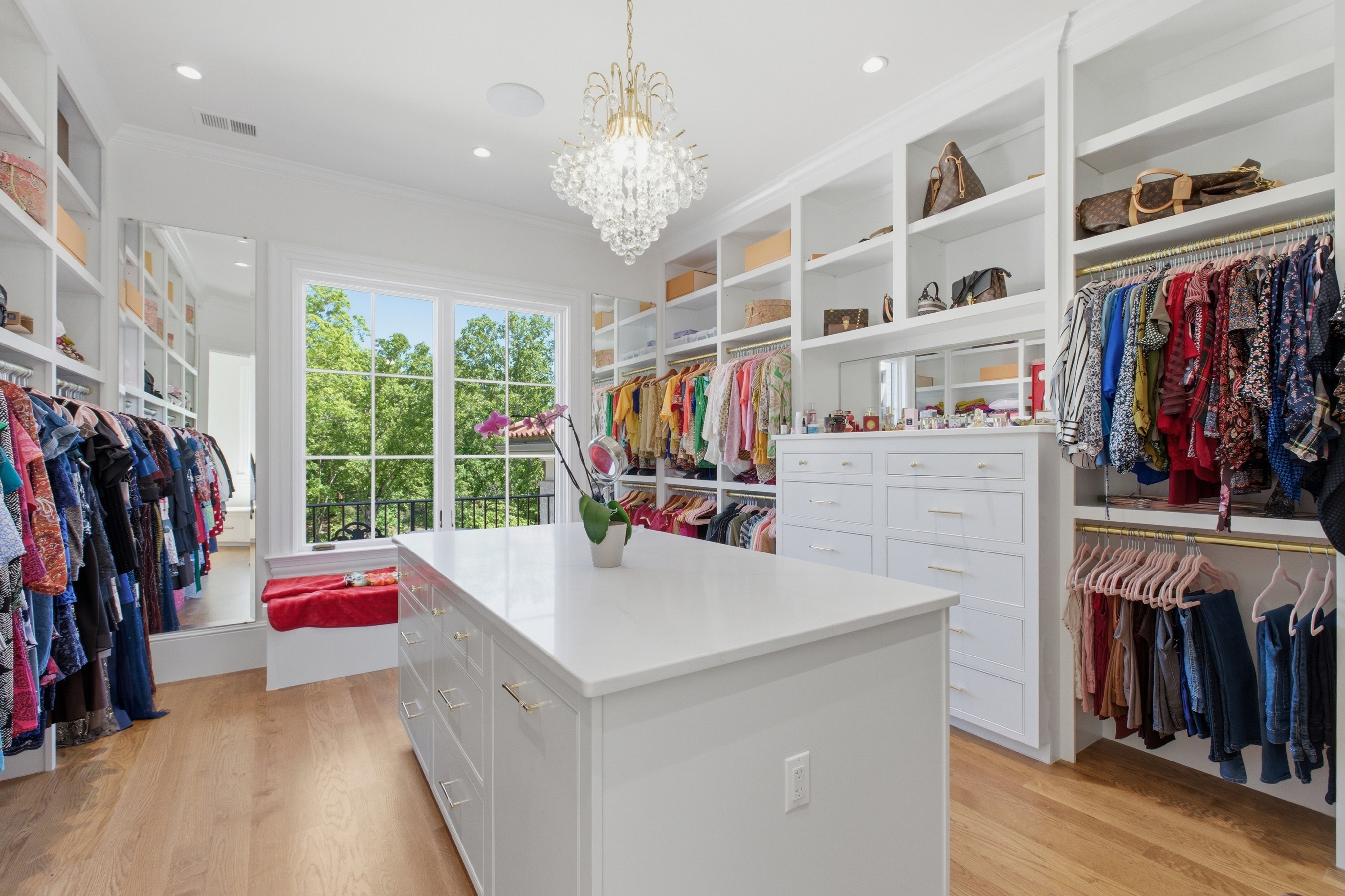 Primary walk-in closet with marble-topped center island, crystal chandelier, and full-wall built-ins